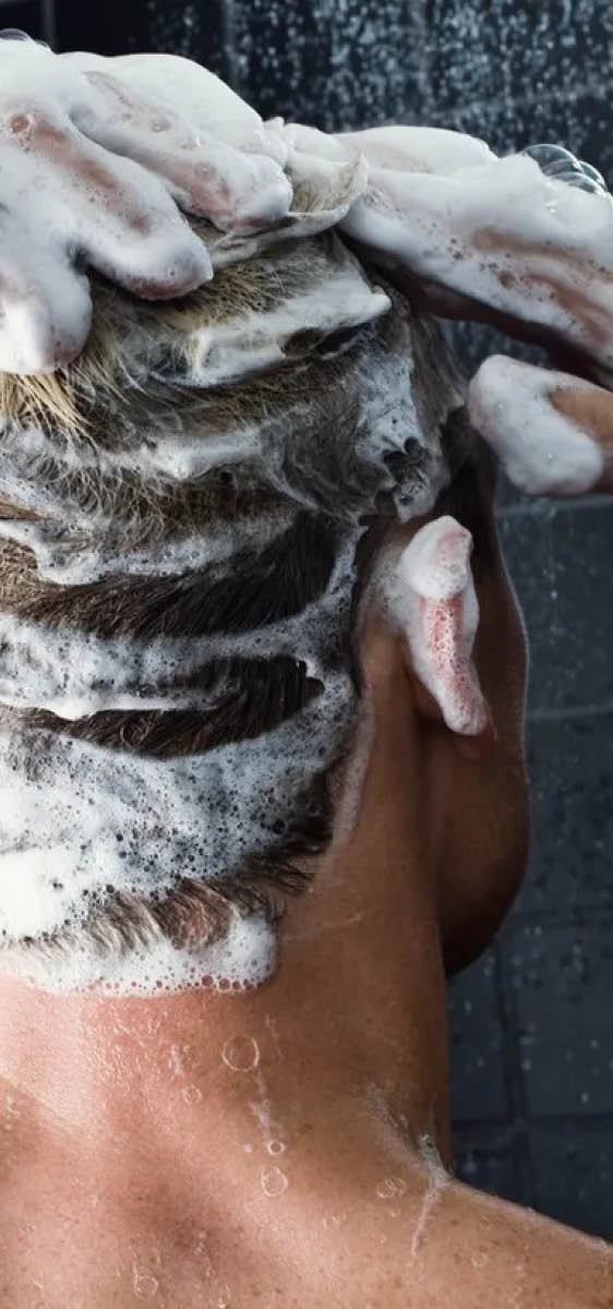 Immagine di un uomo sotto la doccia, visto di spalle, con i capelli molto insaponati